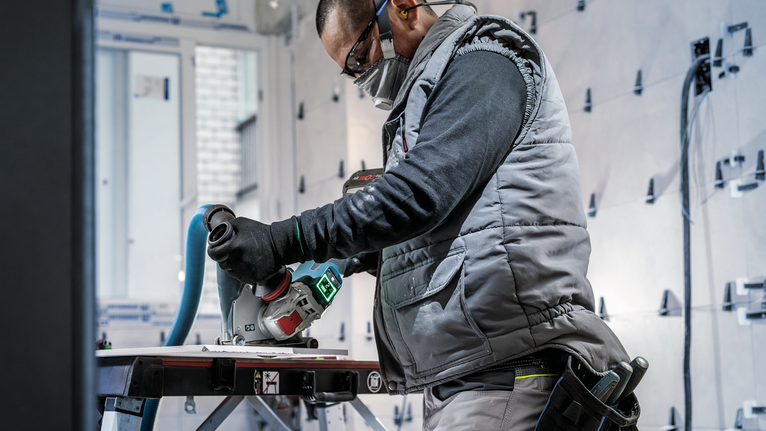 佩戴安全设备的人员使用电动工具在工作台上切割材料。