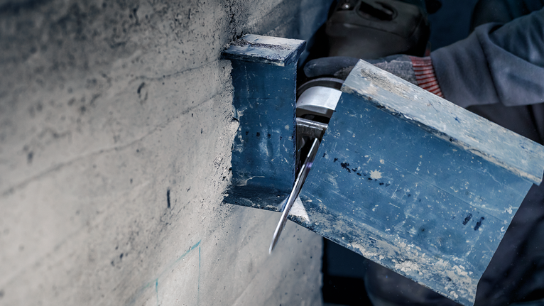 佩戴安全设备的人员使用电动工具切割钢梁。