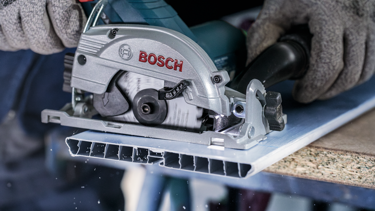 佩戴安全设备的人员用圆锯切割金属板。