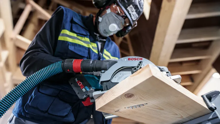 佩戴安全设备的人员用圆锯切割木板。