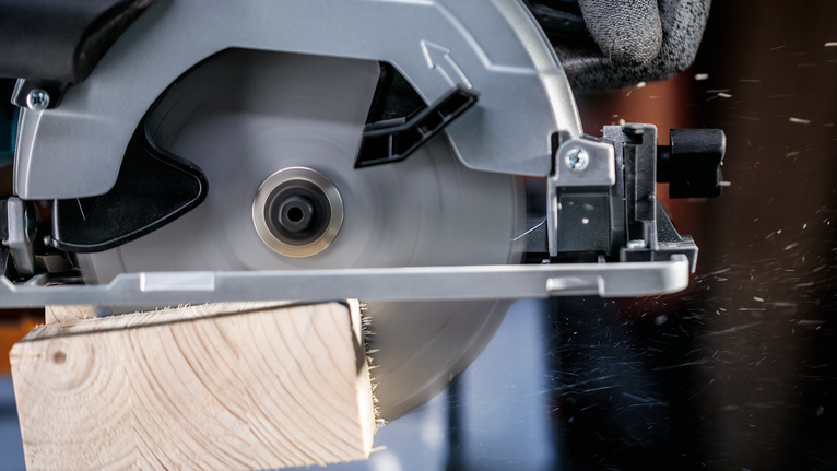 佩戴安全设备的人员用圆锯切割木板。