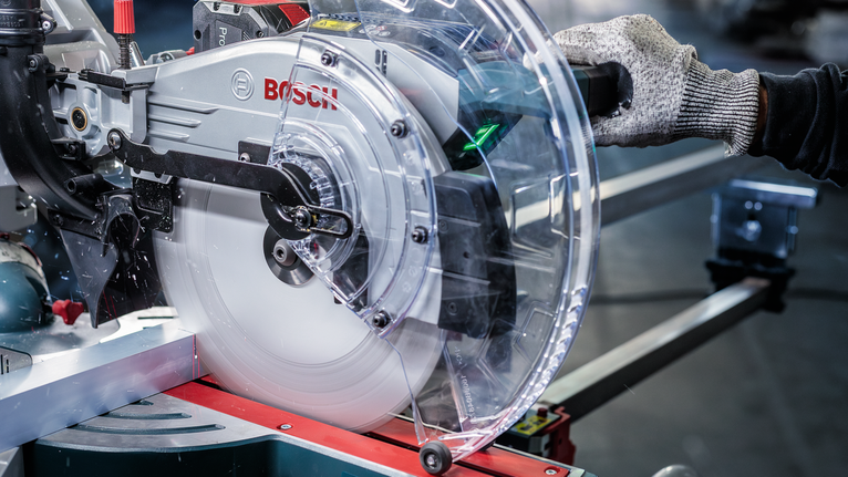 佩戴安全设备的人员在金属切割工作站上操作圆锯。