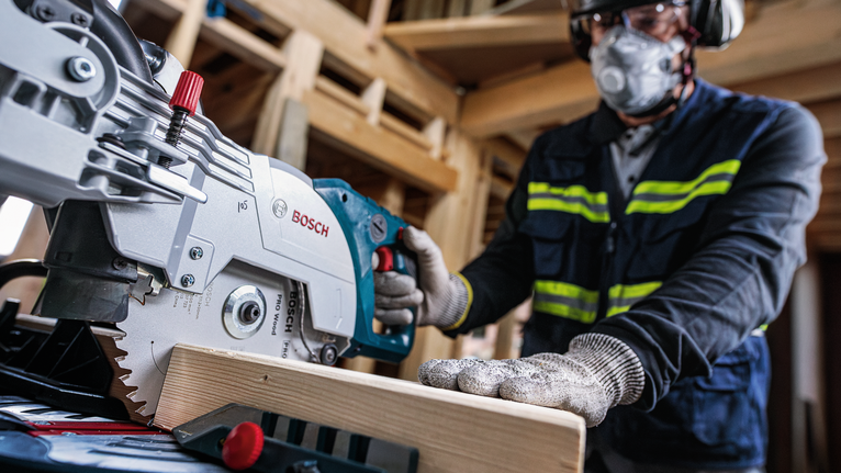 一名佩戴安全设备的人员操作圆锯切割木梁。