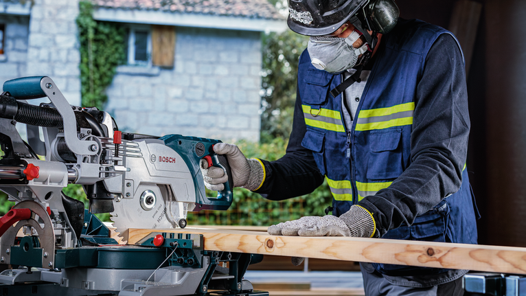 一名佩戴安全设备的人正在用斜切锯切割木板。