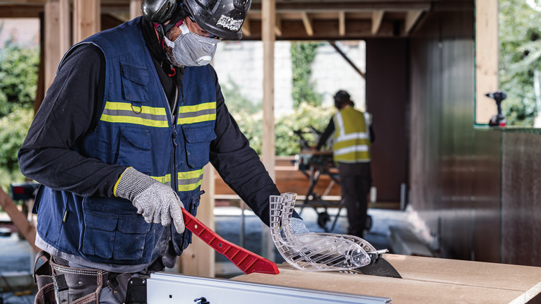 一名佩戴安全设备的人员在建筑工地调整锯片防护装置。