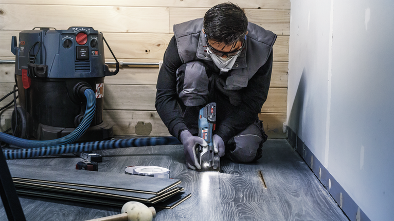 一名佩戴安全设备的人员正在使用电动工具切割复合地板。