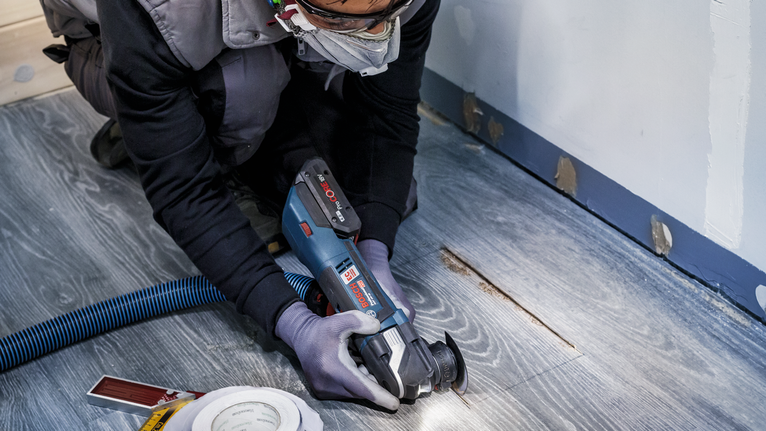 佩戴安全设备的人员使用电动工具切割木地板。