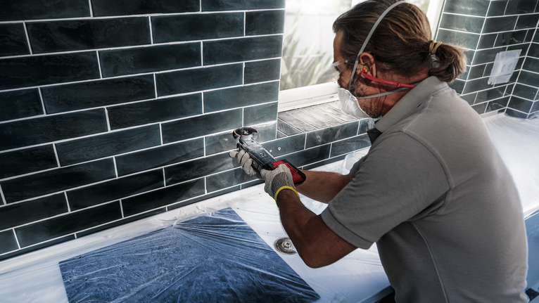 佩戴安全设备的人员使用电动工具切割窗户下方的瓷砖。
