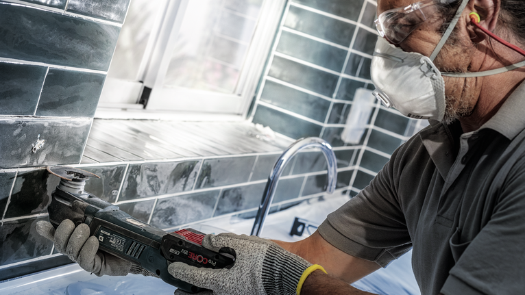 一名佩戴安全设备的人员使用电动工具切割水槽附近的瓷砖。
