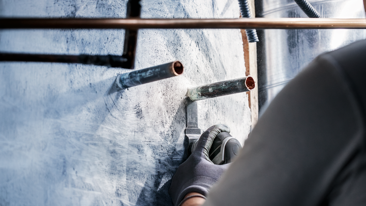 佩戴安全设备的人员使用电动工具切割金属管道周围的墙壁。