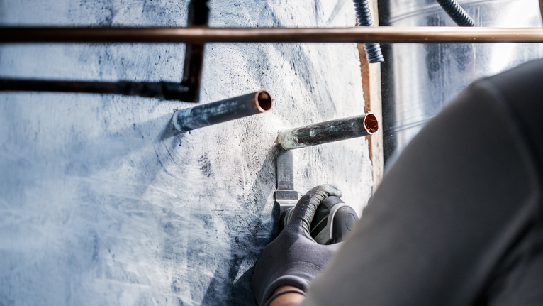 佩戴安全设备的人员使用电动工具切割金属管道周围的墙壁。