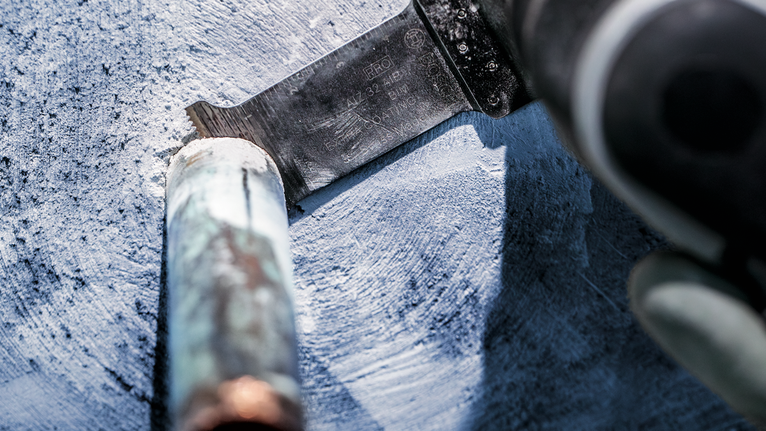 佩戴安全设备的人员使用往复锯切割金属管道。