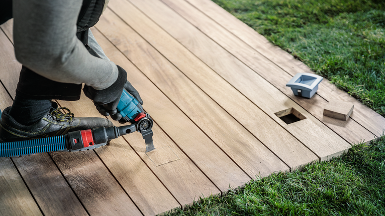 佩戴安全设备的人员使用电动工具切割木质甲板。