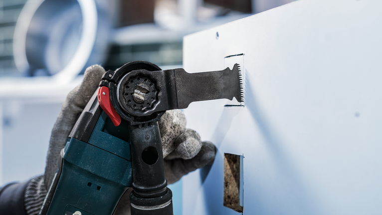 佩戴安全设备的人员使用电动工具在干墙上切出一个矩形孔。