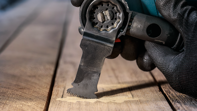 佩戴安全设备的人使用多功能工具切割木材。