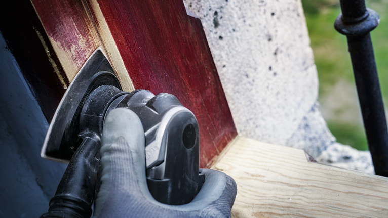 一名佩戴安全设备的人员正在使用电动工具打磨涂漆的木材。