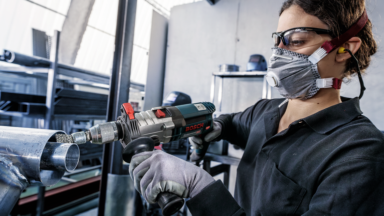 佩戴安全设备的人员使用电动工具研磨金属管的末端。