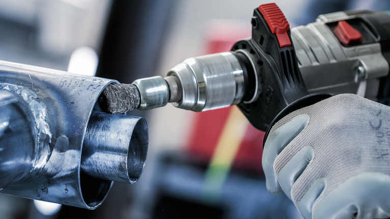 佩戴安全设备的人员使用电钻打磨金属管道内部。