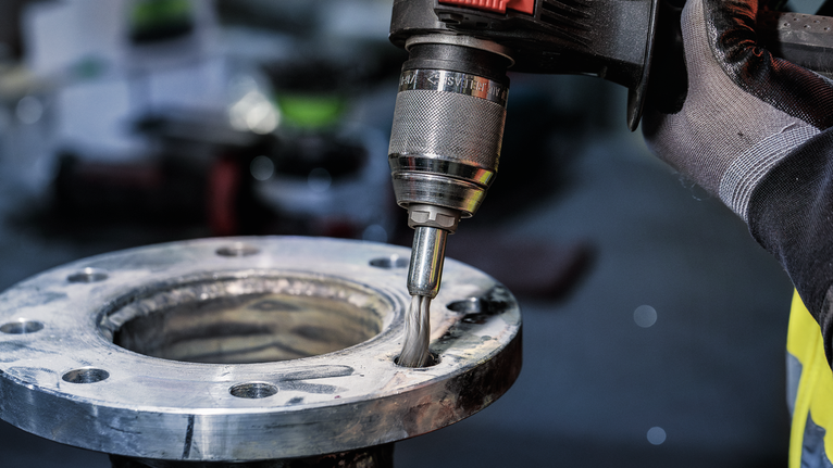 佩戴安全设备的人员使用电动工具抛光金属法兰的内部。