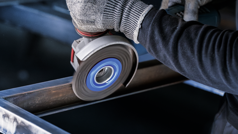 佩戴安全设备的人员使用角磨机打磨钢梁。