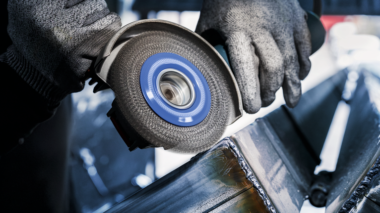 佩戴安全设备的人员使用角磨机打磨金属梁。