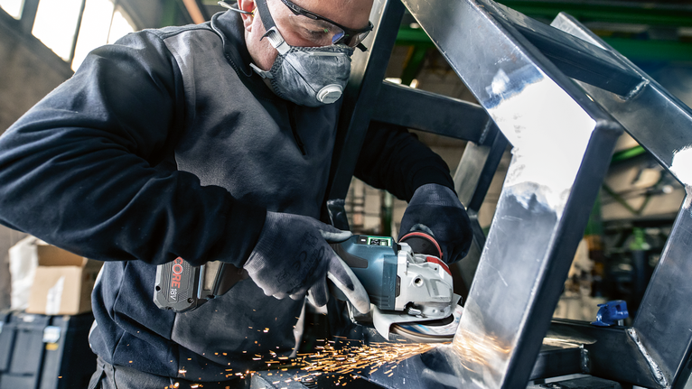 一名佩戴安全设备的人研磨金属框架，产生火花。