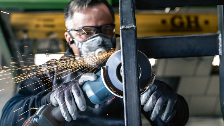 佩戴安全设备的人研磨金属，产生火花。