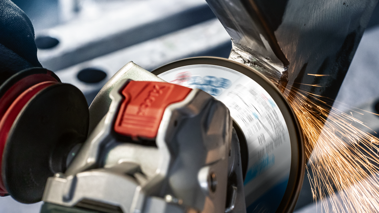 一名佩戴安全设备的人用角磨机研磨金属，产生火花。