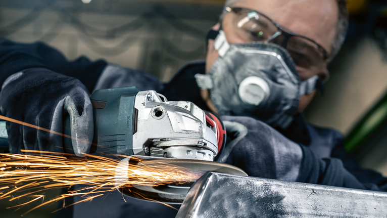 一名佩戴安全设备的人研磨金属，产生明亮的火花。