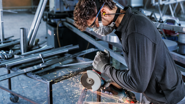 佩戴安全设备的人使用角磨机切割金属，产生火花。