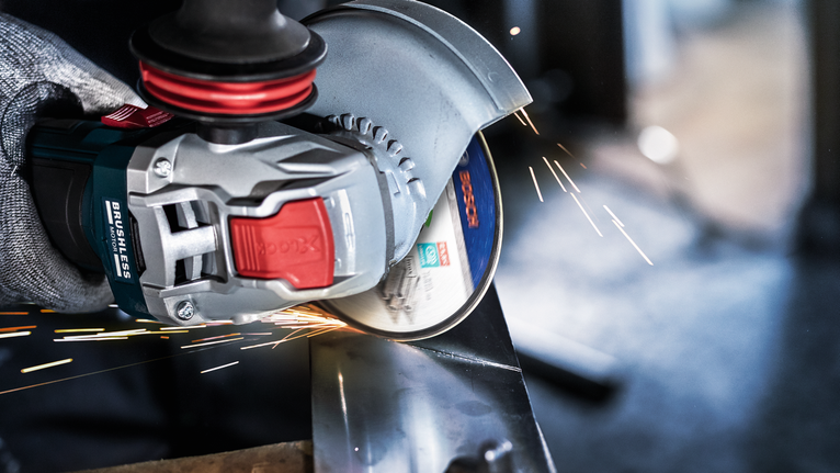 一名佩戴安全设备的人研磨金属，产生明亮的火花。