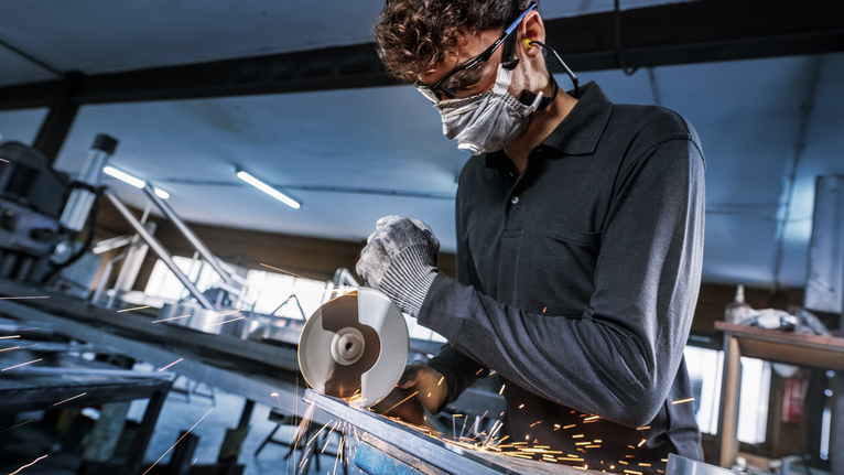 佩戴安全设备的人用角磨机切割金属，火花四溅。