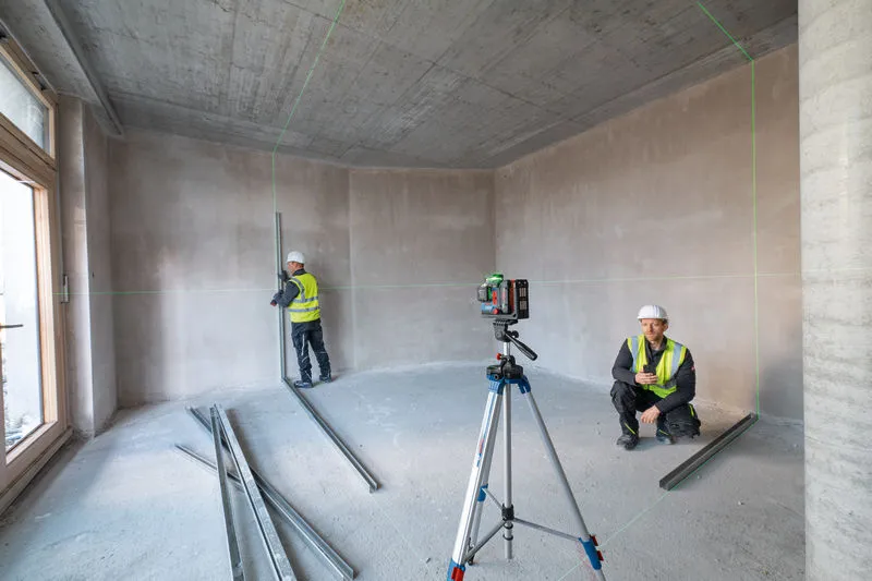 两名佩戴安全设备的人员在未完工的房间里使用激光调平工具。