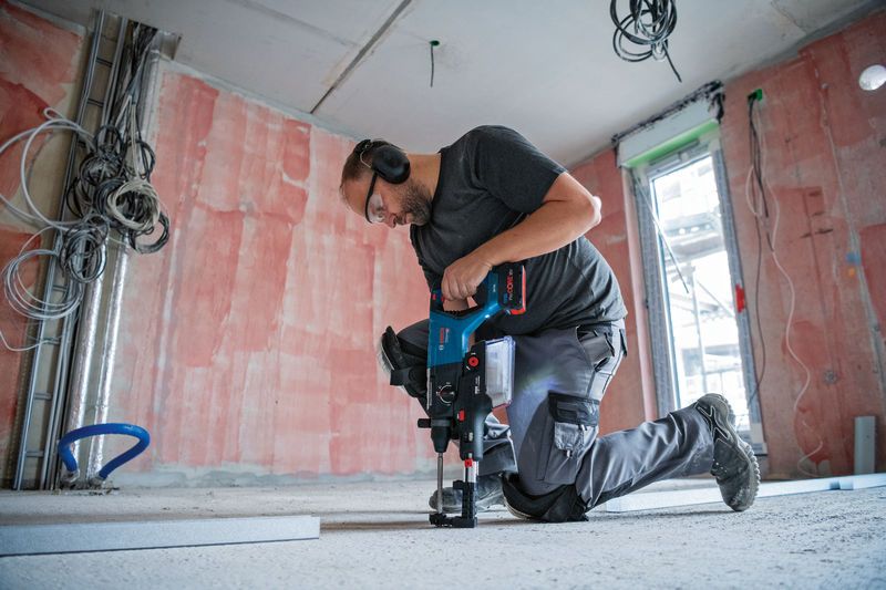 一名佩戴安全设备的人员使用无绳旋转锤在混凝土地板上钻孔。.