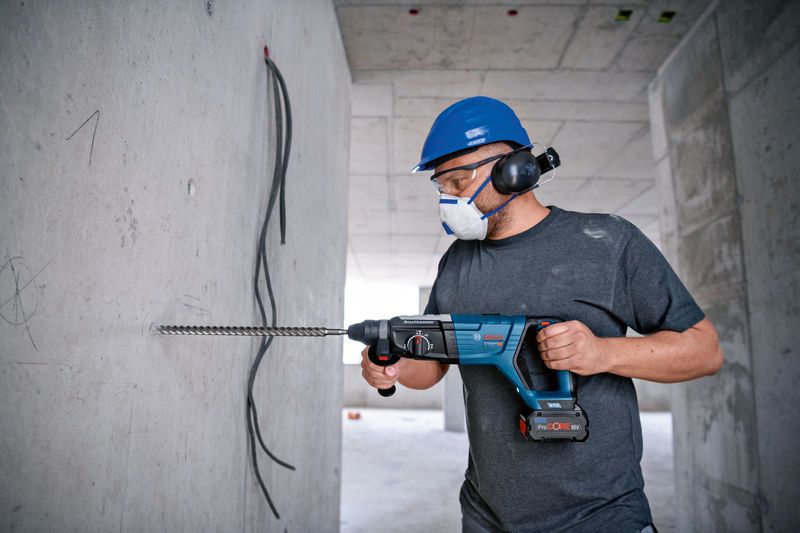 一名佩戴安全设备的人员使用旋转锤在混凝土墙上钻孔。.