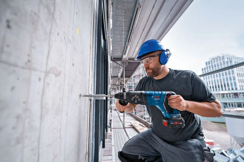 一名佩戴安全设备的人员使用旋转锤在混凝土墙上钻孔。.