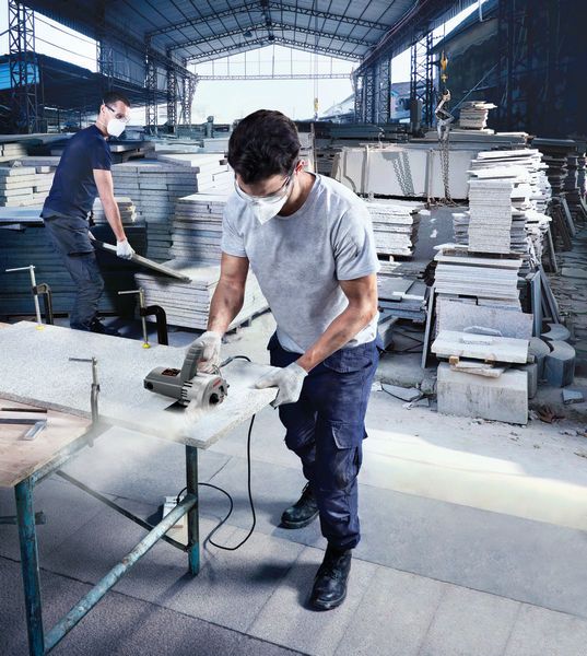 佩戴安全设备的人员在室内使用大理石锯切割石板。.