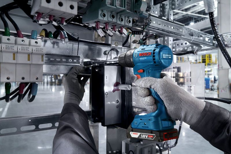 一名佩戴安全设备的人员使用无绳电钻在电气面板上工作。.