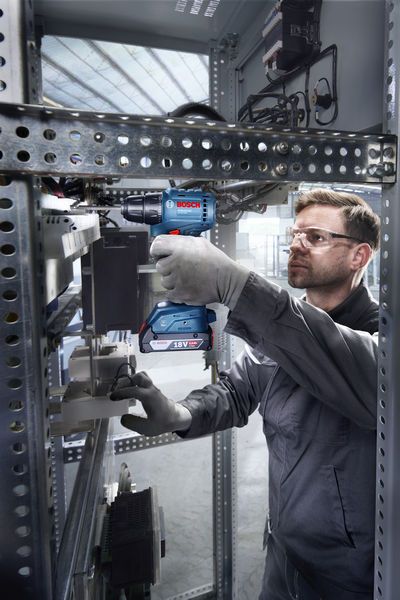 一名佩戴安全设备的人员在电气柜内使用无绳电钻。.