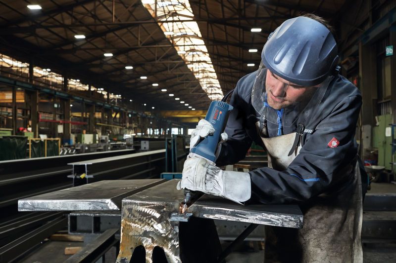 一名佩戴安全设备的人员使用直磨机打磨金属梁。.