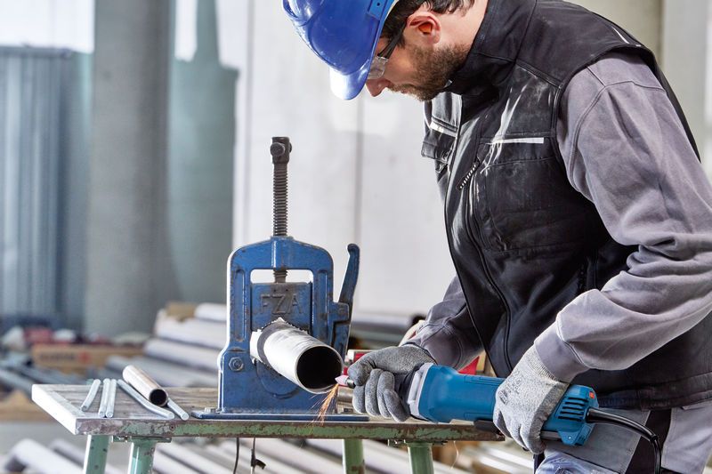 一名佩戴安全设备的人员使用直磨机对金属管道进行加工。.