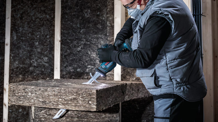 佩戴安全设备的人员使用往复锯切割绝缘材料。