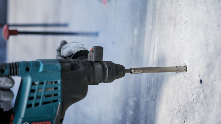 一名佩戴安全设备的人员使用旋转锤在混凝土中钻孔。