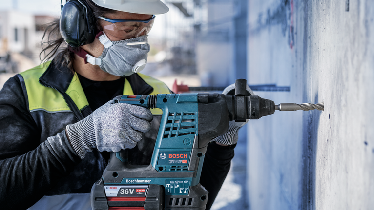 佩戴安全设备的人员使用旋转锤在混凝土墙上钻孔。