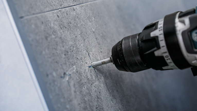 钻头在灰色瓷砖墙上打出一个精确的孔。