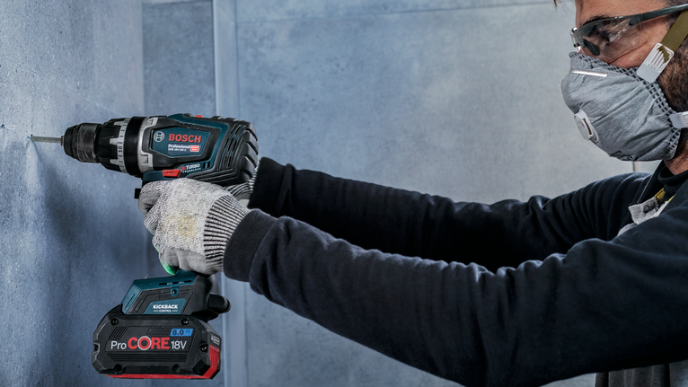一名佩戴安全设备的人正在钻入混凝土墙。