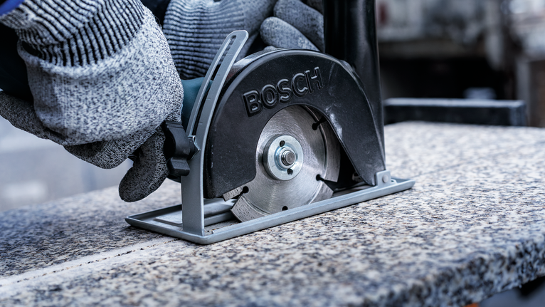 一名佩戴安全设备的人员使用金属锯切割花岗岩板。