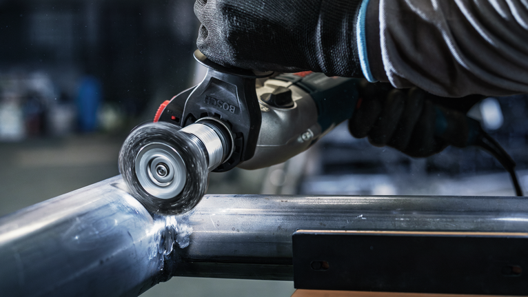 佩戴安全设备的人员使用电动工具抛光金属管。