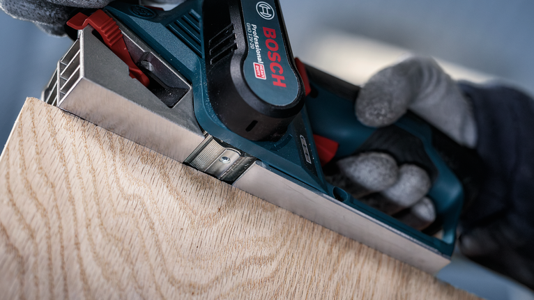 穿着安全装备的人刨木板的边缘。