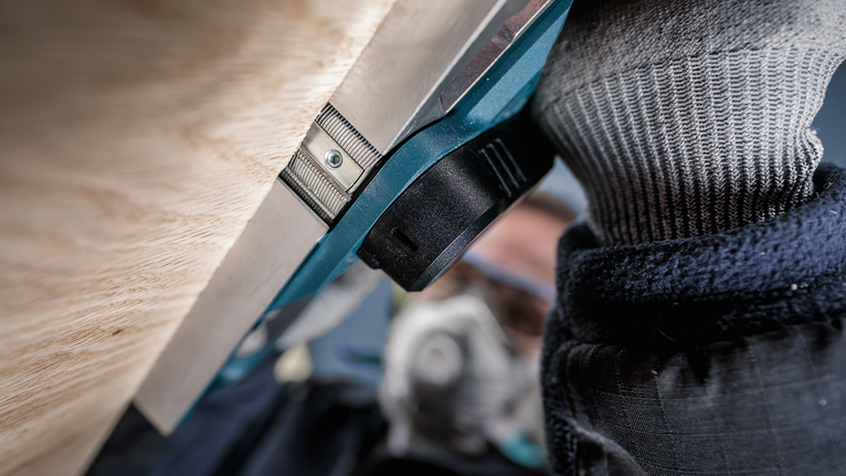 佩戴安全设备的人员在靠近木质表面的地方操作电动工具。